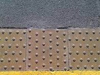 The image shows an example of brown tactile pavement, that is small raised dots on a pavement, there is also a yellow band of paint, further used to highlight a crossing. 